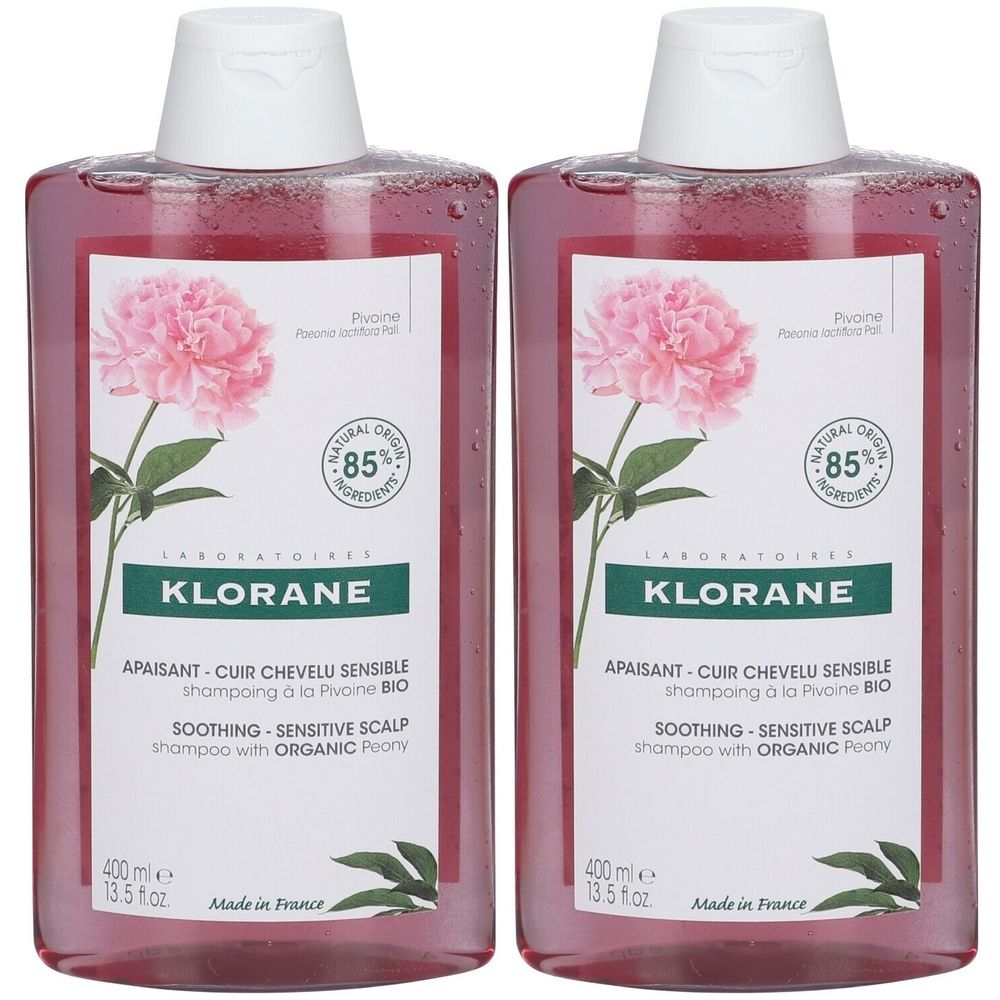 Twee flessen Klorane shampoo. Roze vloeistof, witte dop. Etiket met pioenroos, tekst: 85% ingrediënten, verzachtend, gevoelige hoofdhuid.