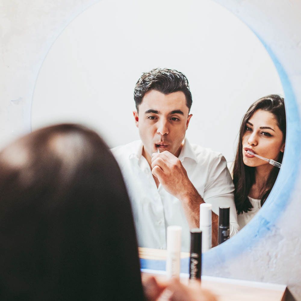 Couple se brossant les dents dans le miroir. Dentifrice et marque non visibles.