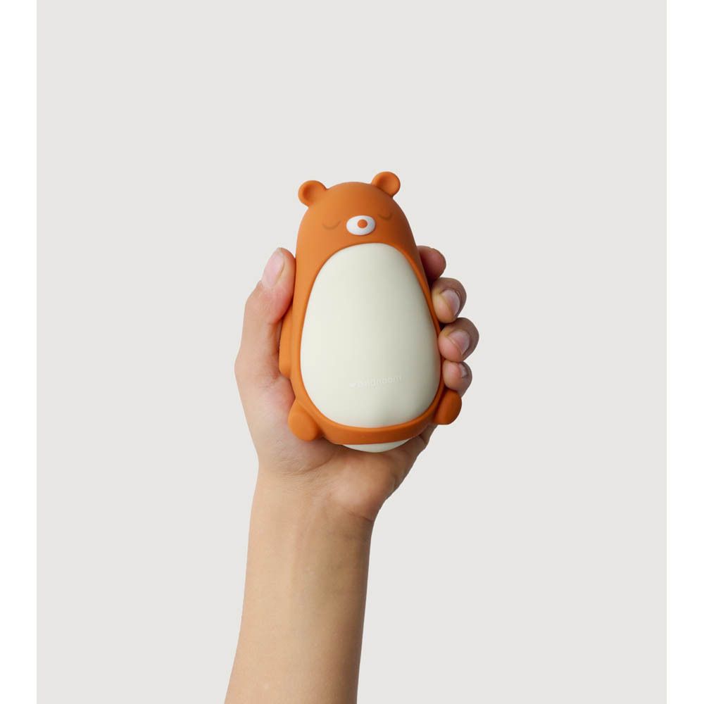 Moonbird Moonbuddy Barry l'ours, oranje en wit. Vastgehouden in een hand, in bed.