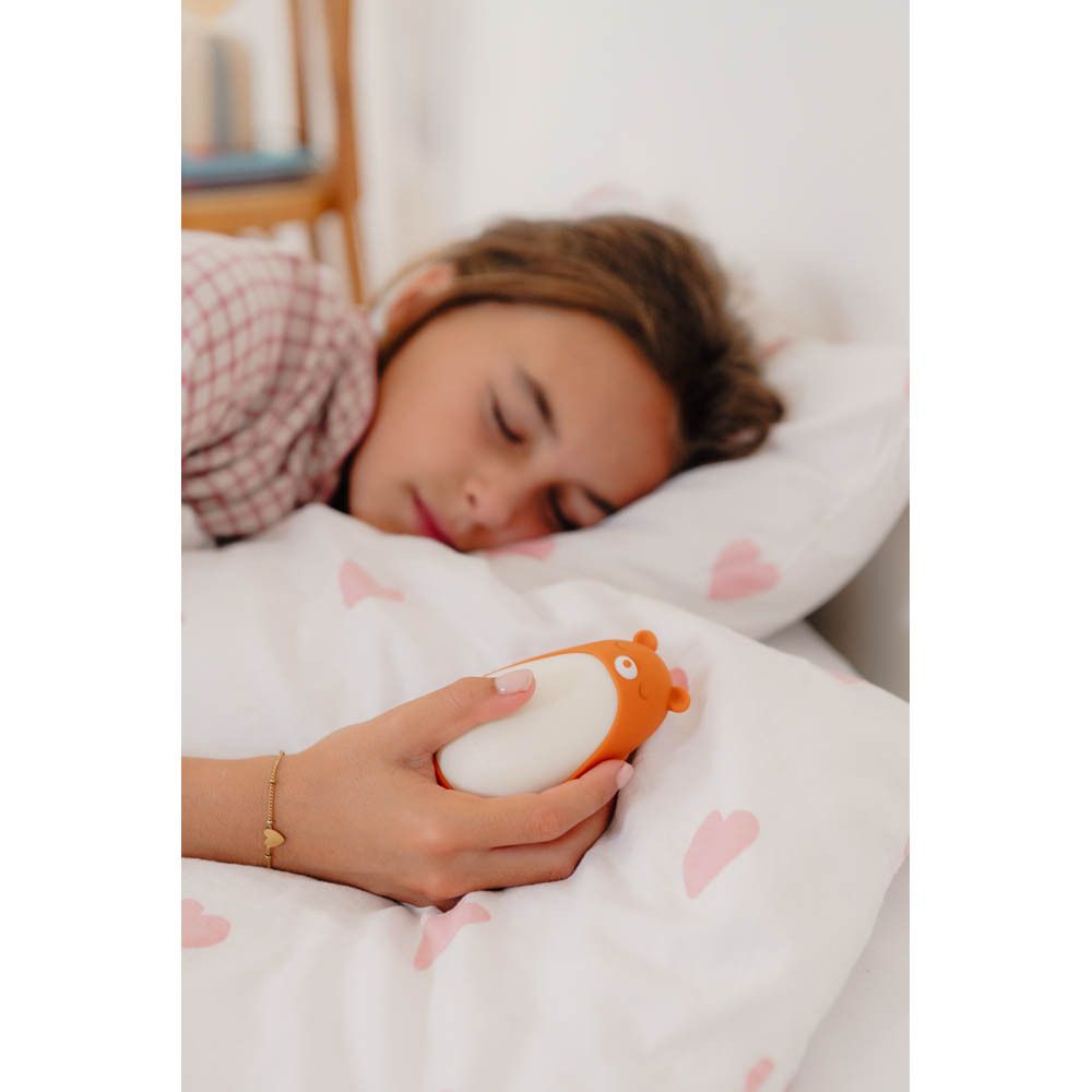 Moonbird Moonbuddy Barry l'ours, oranje en wit. Vastgehouden in een hand, zittend op een bank.