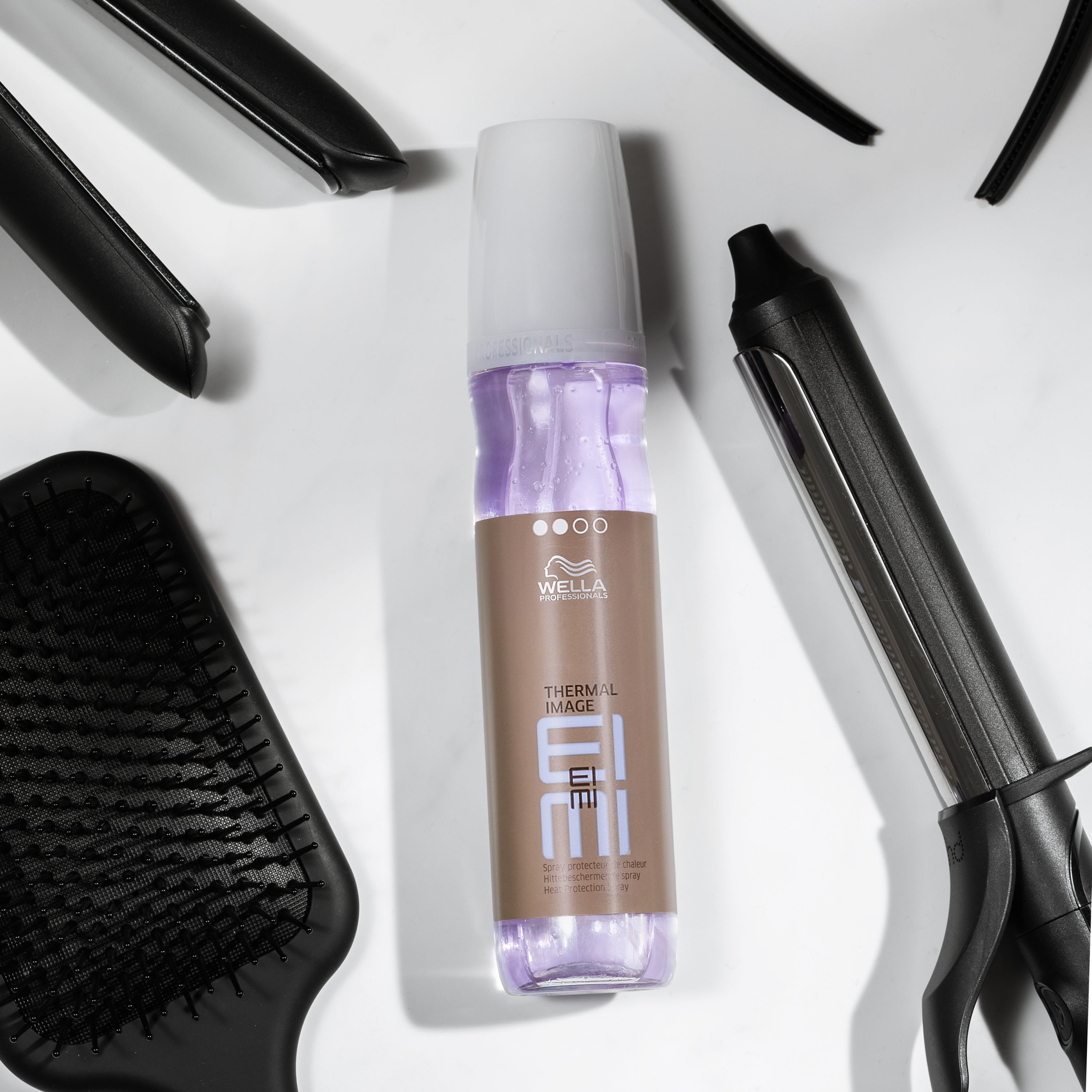 Spray protecteur thermique Wella EIMI. Produit avec accessoires de coiffure sur fond blanc.