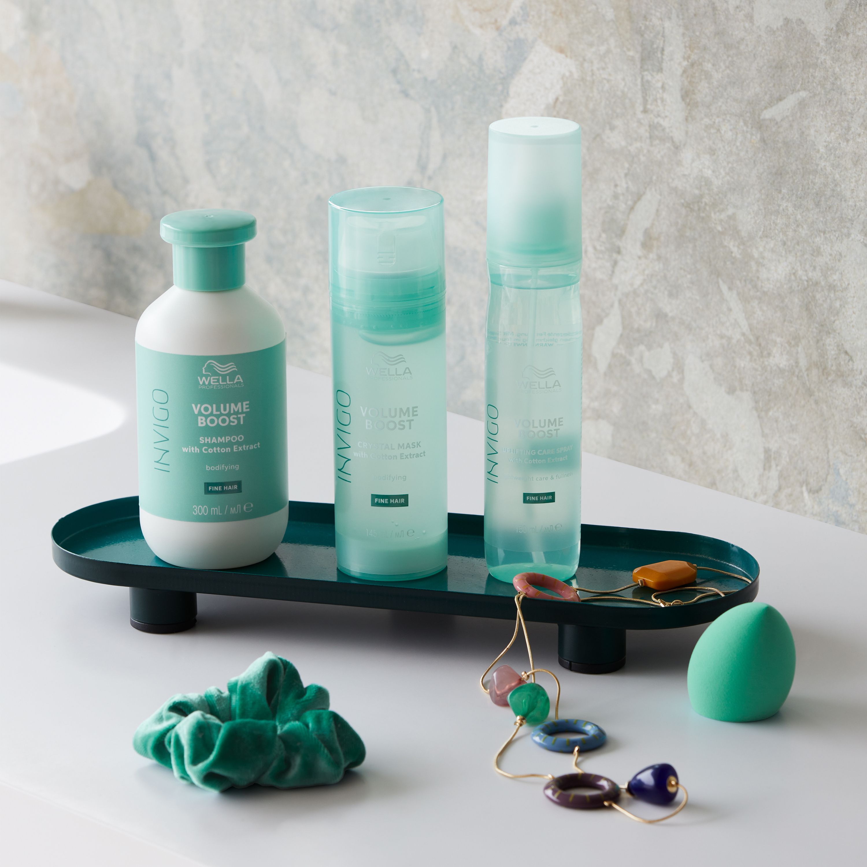 Productarrangement met shampoo fles, sprays, haar elastiek, sieraden en spons op dienblad.