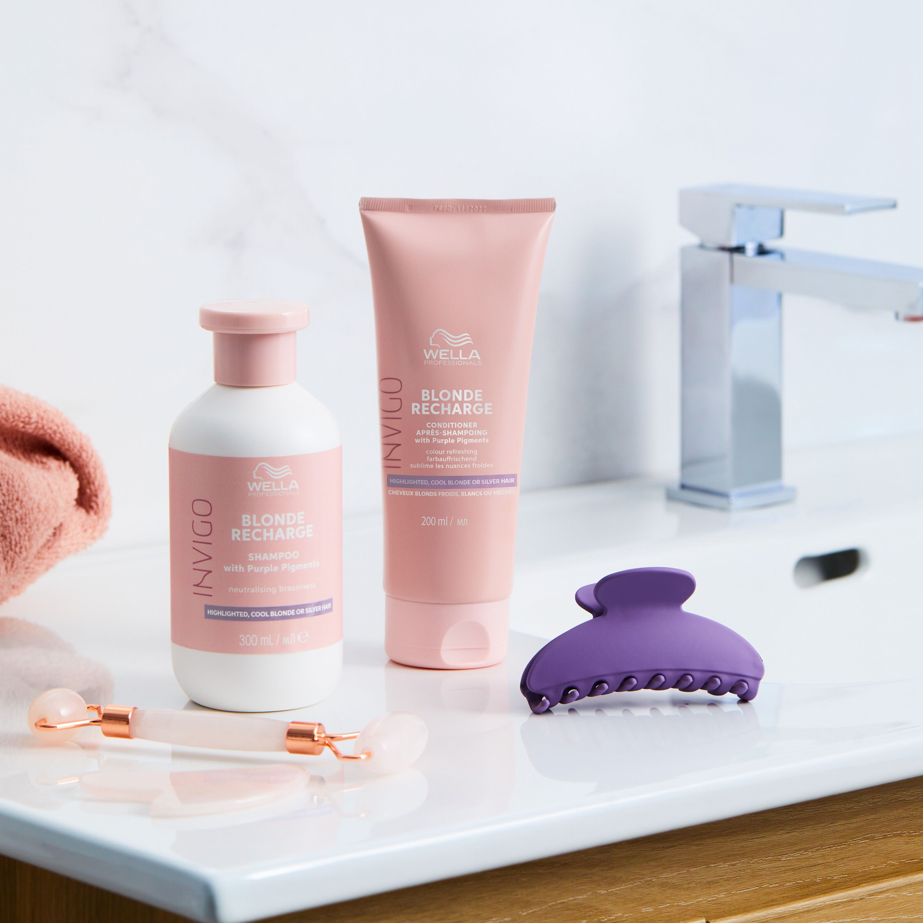 Productset op wastafel. Wella Invigo Blonde Recharge Shampoo en conditioner, haarclip, gezichtsroller.