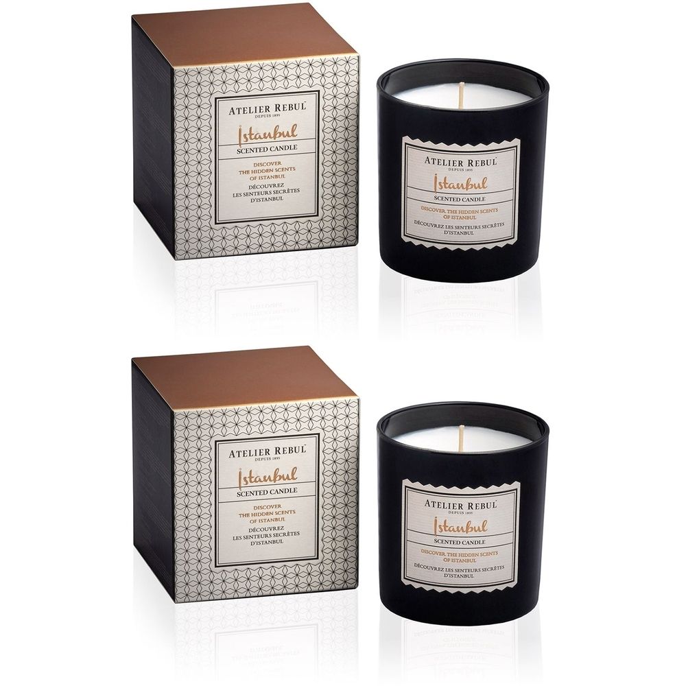 Twee zwarte kaarsen met witte was en etiket. Daarnaast twee vierkante dozen met gouden deksel en etiket.