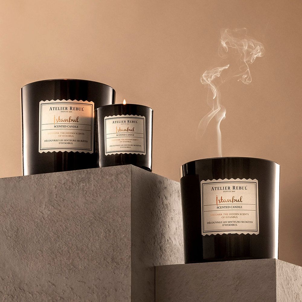 Trois bougies parfumées noires de différentes tailles, dont une allumée, avec de la fumée.