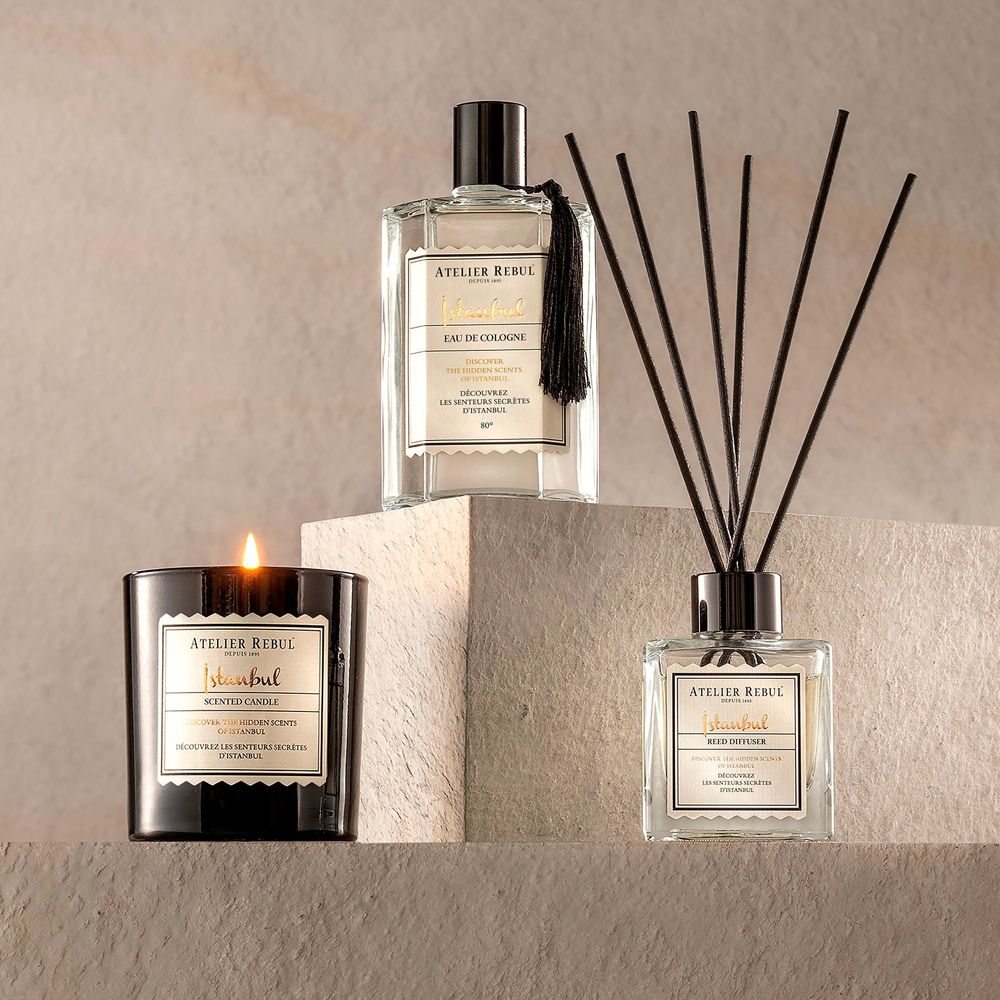 Bougie parfumée, eau de Cologne et diffuseur à bâtonnets présentés en arrangement.