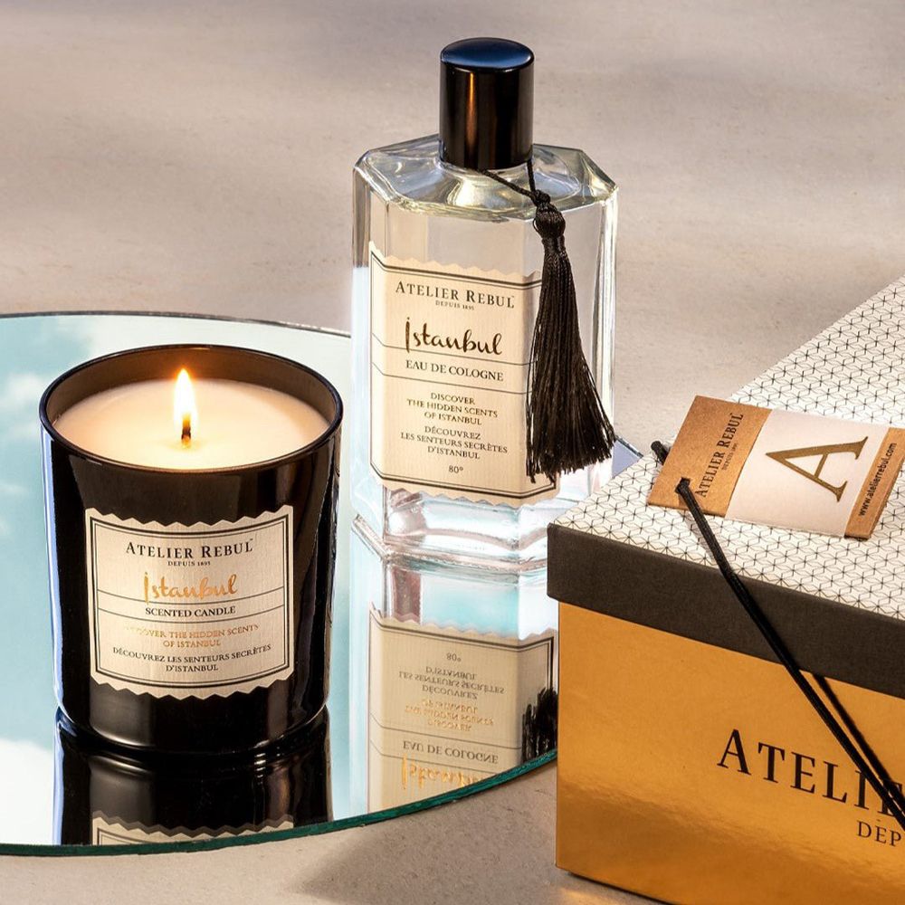 Bougie parfumée allumée et eau de Cologne sur un miroir, à côté d'une boîte cadeau.