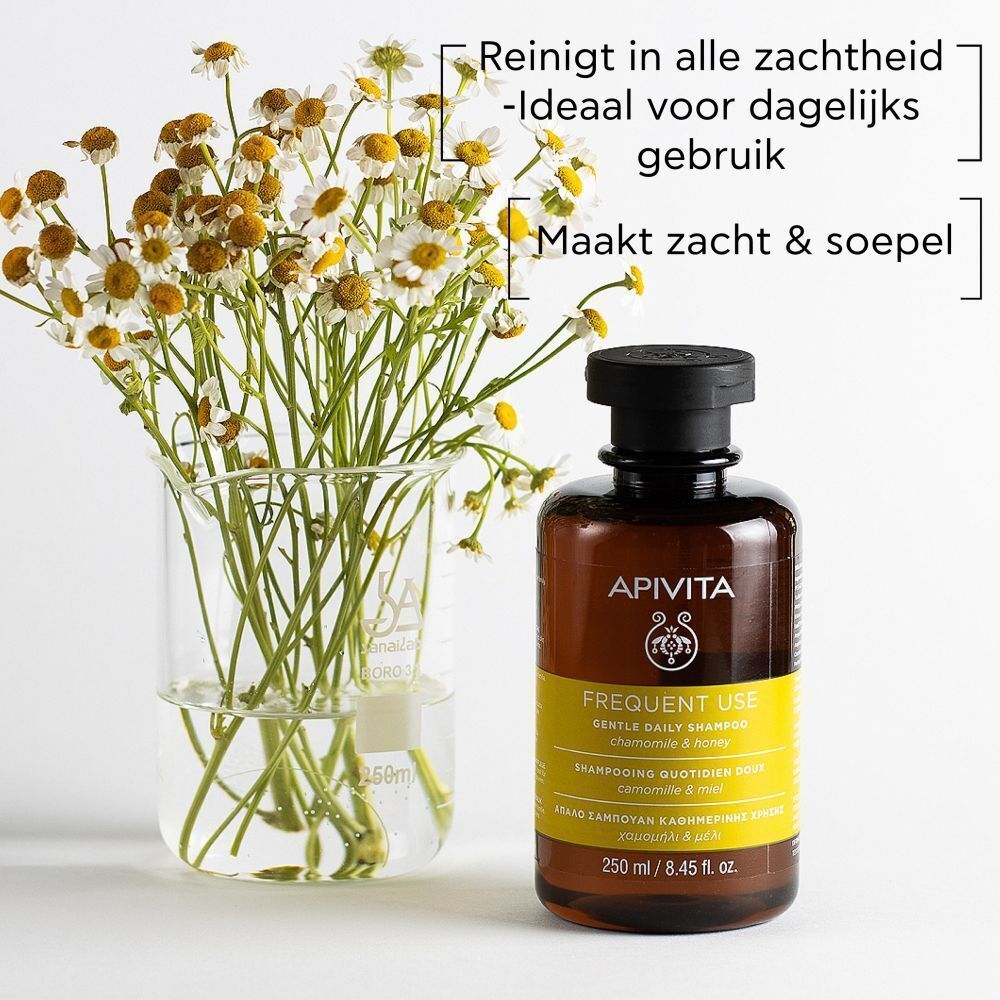 Shampoo fles naast kamillebloemen in een bekerglas. Tekst: Reinigt in alle zachtheid, Ideaal voor dagelijks gebruik, Maakt zacht & soepel.