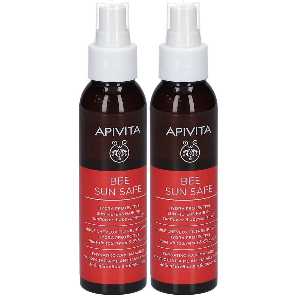 Twee flessen met verstuiver. Opschrift: Apivita, Bee Sun Safe. Rode sticker met tekst. Bruine vloeistof zichtbaar.