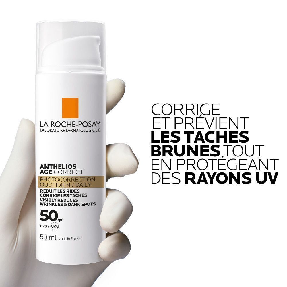 Une main gantée tient un flacon de La Roche-Posay Anthelios Age Correct SPF50.
