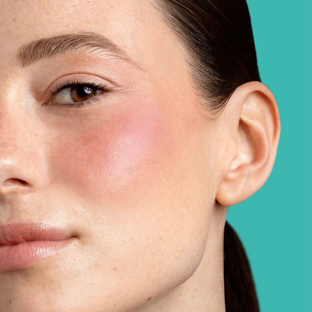 Close-up van een gezicht met blush op de wang. Huidtint, bruine ogen, donker haar.