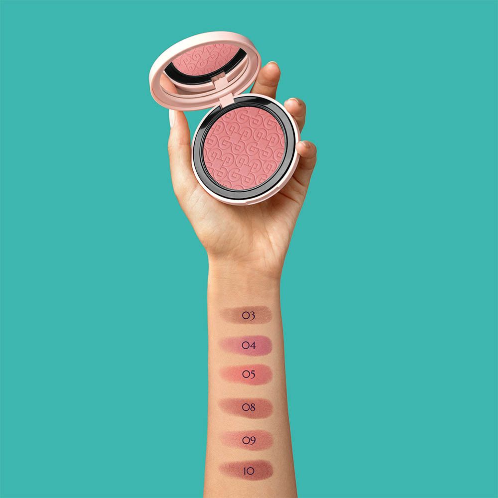 Hand houdt een open blush compactpoeder vast. Kleurstalen van blush aangebracht op de arm, genummerd van 03 tot 10.
