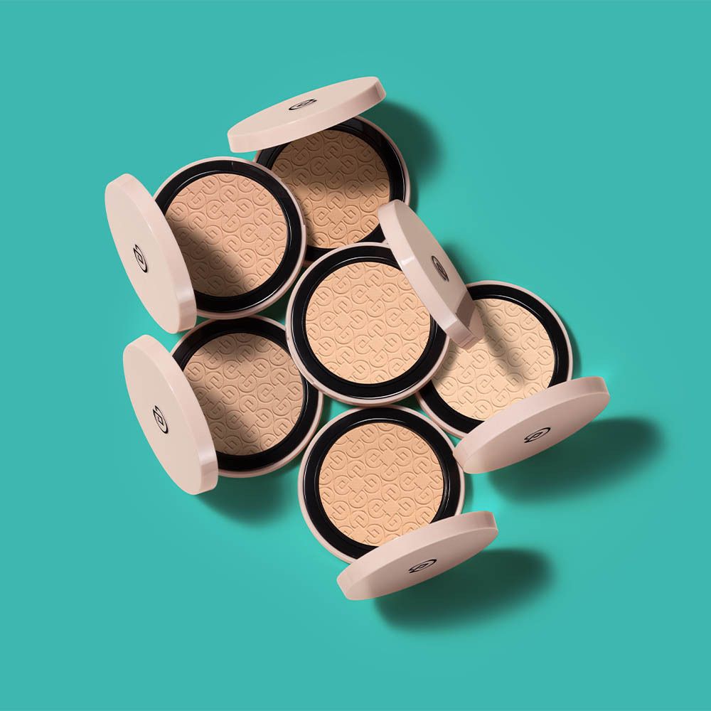 Meerdere Collistar Impeccabile Compact Powders. Open poederdozen, roze deksels, beige poeder, op blauwe achtergrond.