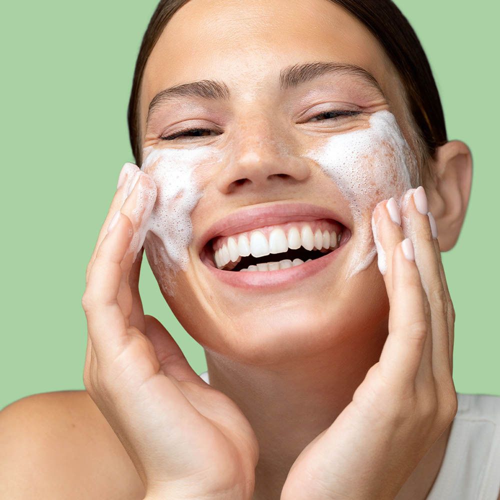 Close-up van een gezicht met schuim. Persoon glimlacht. Product: Cleansing Cream To Mousse.