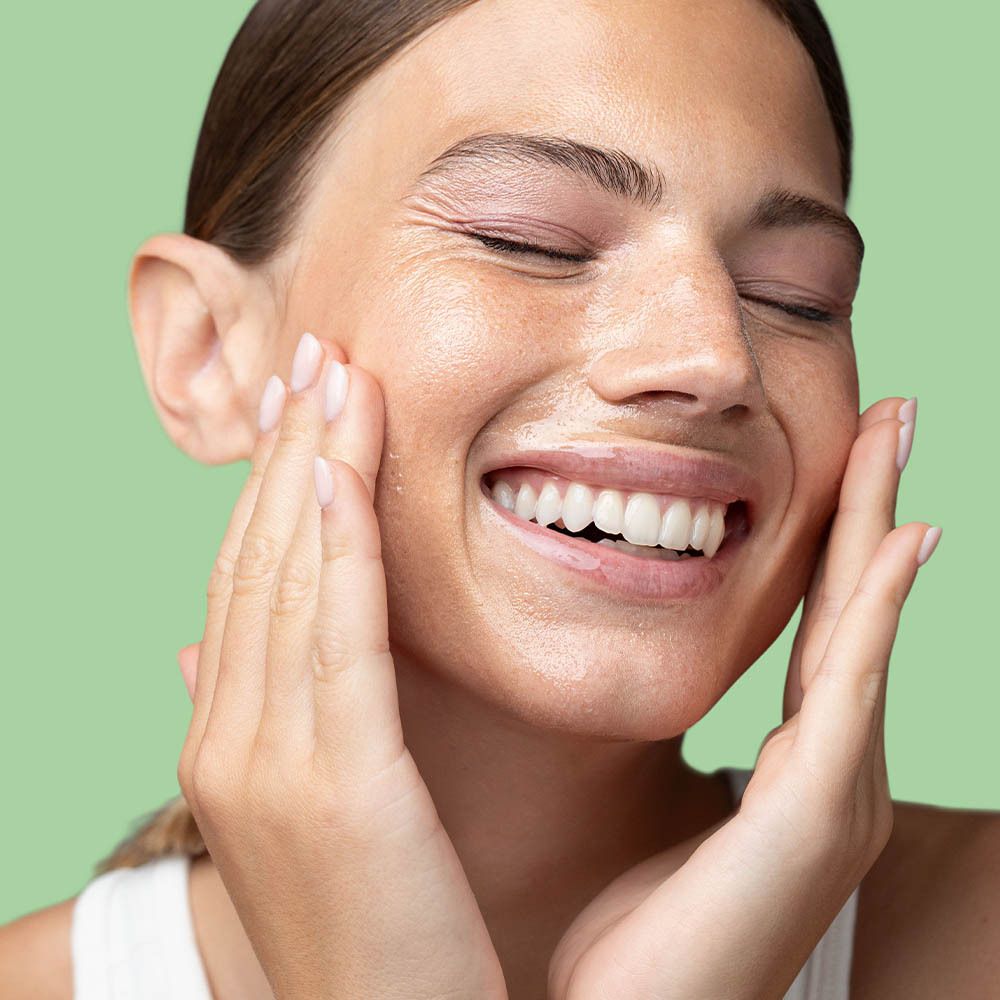 Vrouw met gesloten ogen die olie op haar gezicht aanbrengt. Groene achtergrond.