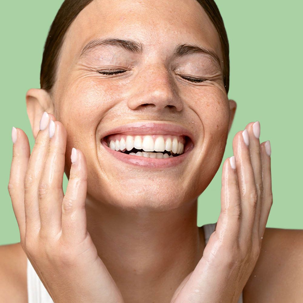 Vrouw met gesloten ogen die olie op haar gezicht aanbrengt. Groene achtergrond.