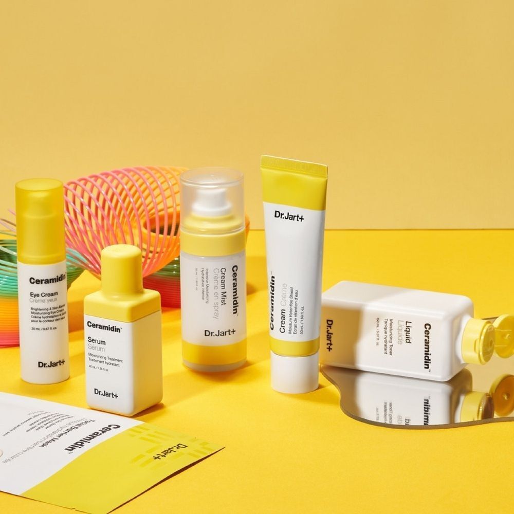 Gele achtergrond met Dr.Jart+ Ceramidin producten. Inclusief: masker, crème, serum, mist en oogcrème.