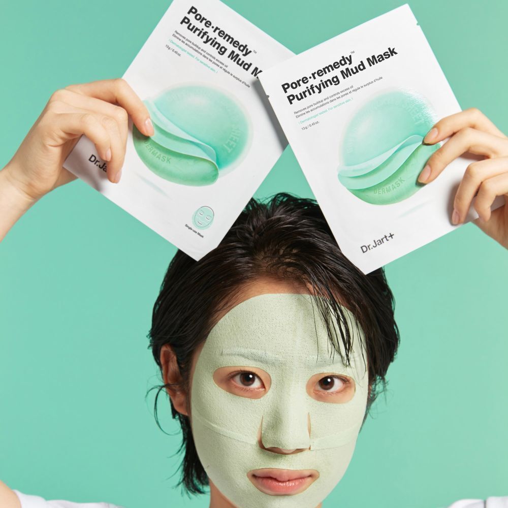 Personne tenant deux paquets de masques. Inscription : Pore·remedy Purifying Mud Mask. La personne porte un masque facial.