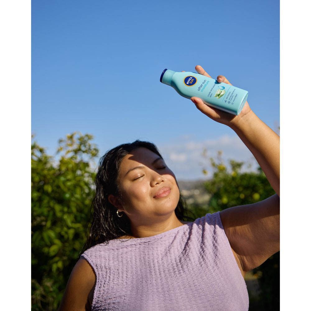 Een vrouw houdt een blauwe fles NIVEA SUN After Sun Lotion vast. Ze lacht. Achtergrond: blauwe lucht.