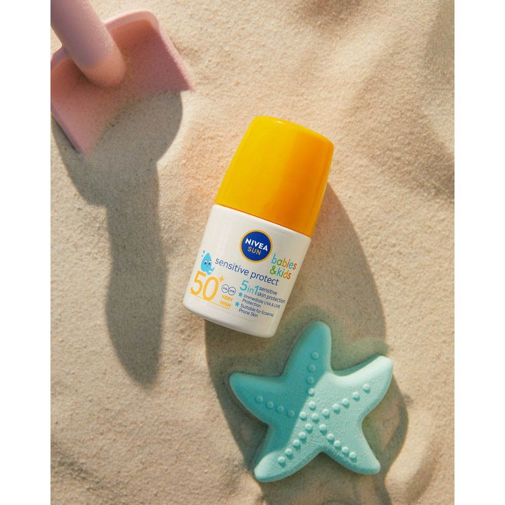 Flacon roll-on avec bouchon jaune sur sable. Inscription: NIVEA SUN babies & kids sensitive protect 50+.