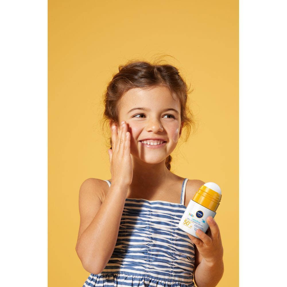 Une fille applique de la crème solaire. Flacon roll-on avec bouchon jaune. Inscription: NIVEA SUN babies & kids sensitive protect 50+.