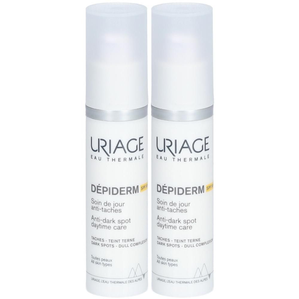 Twee witte flacons Uriage Dépiderm SPF50+ met pomp. Opschrift: Anti-Taches, Soin de Jour, alle huidtypen.