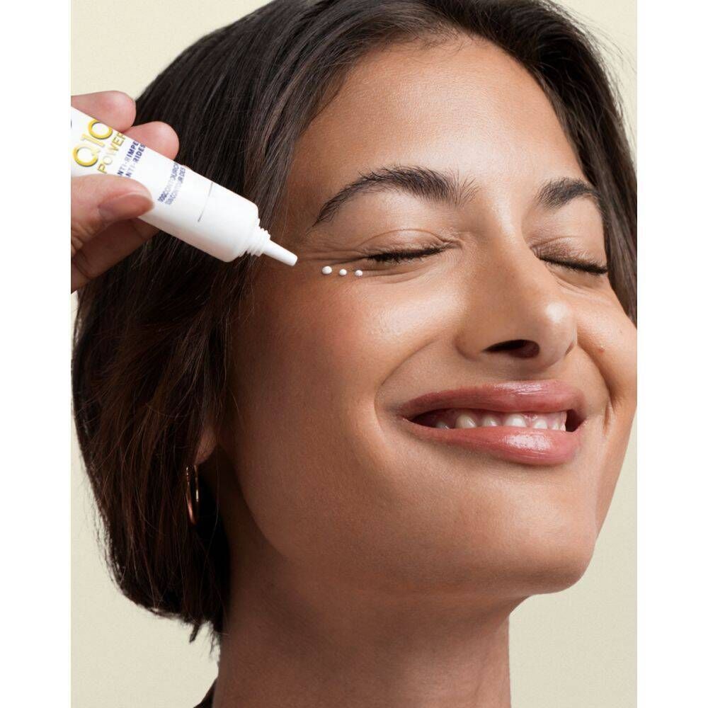 Vrouw met gesloten ogen, product wordt aangebracht. Witte tube met blauw en geel logo. Tekst: Q10 Power, Anti-rimpel, Oogcontourcrème.
