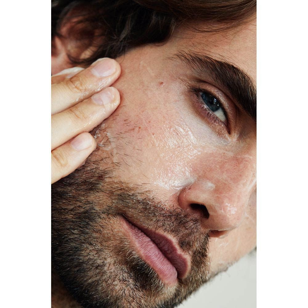 Man brengt crème aan op zijn gezicht. Close-up, huid bedekt met crème.