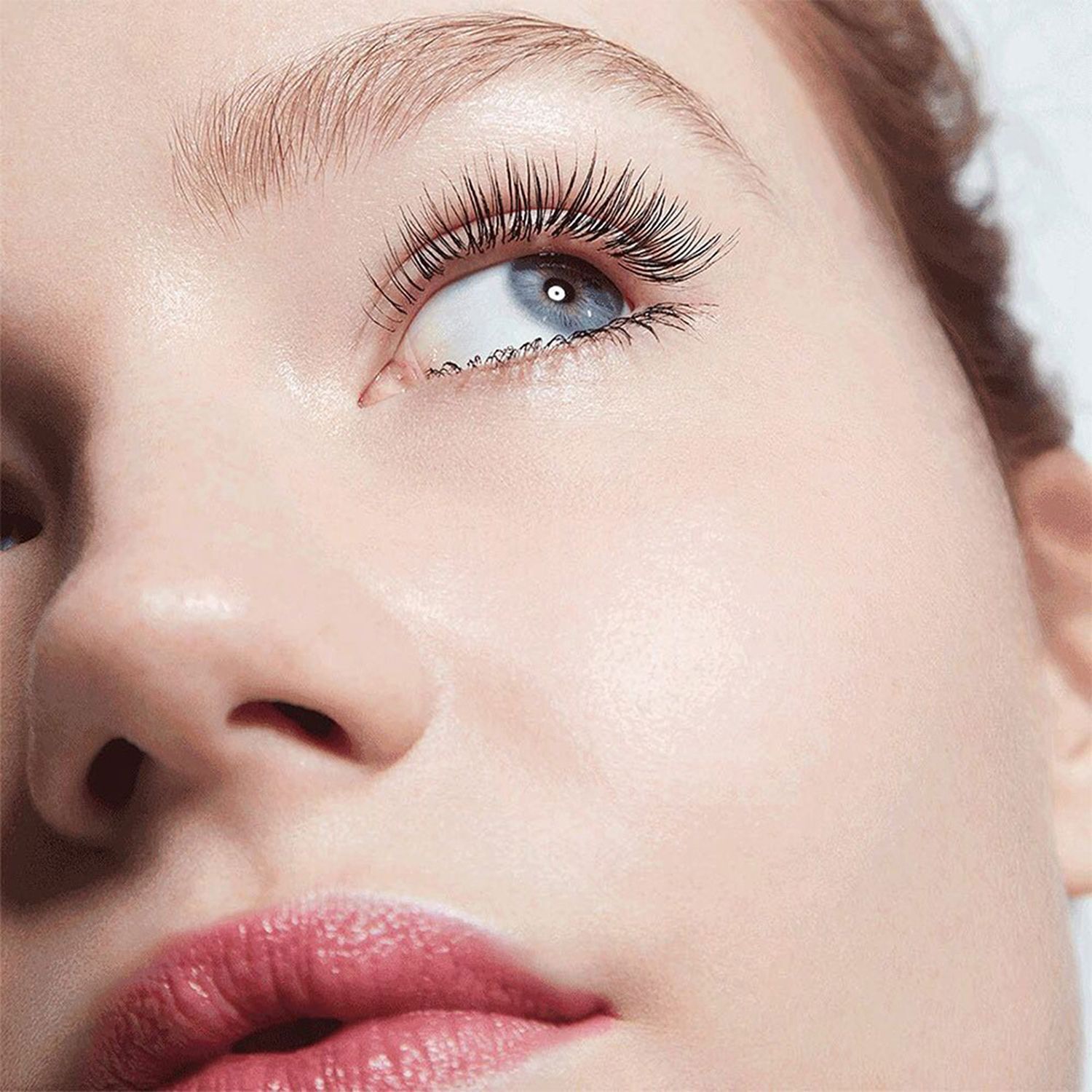 Close-up van een gezicht met lange, met mascara bewerkte wimpers. Rode lippenstift. Blik omhoog.