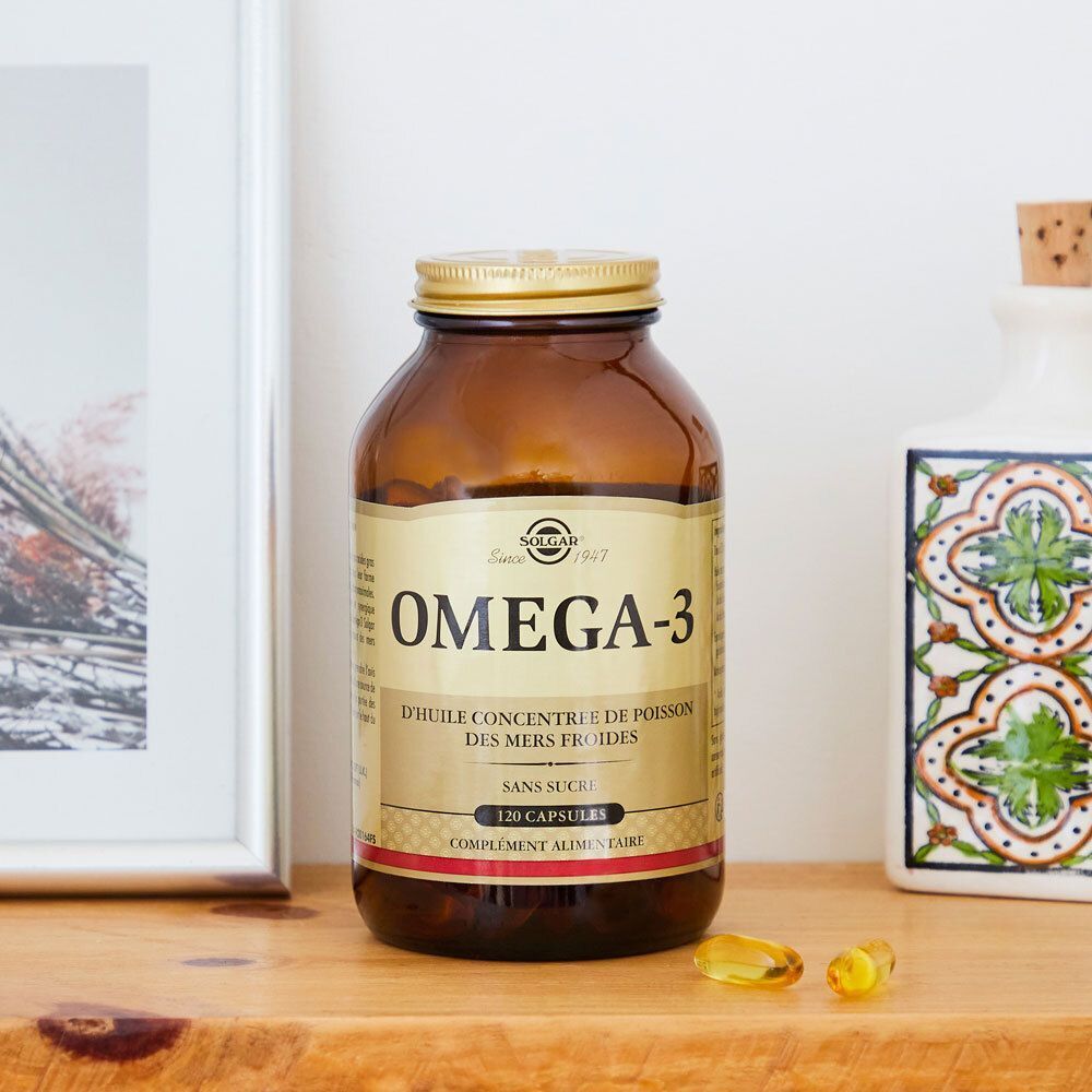Flacon en verre brun avec bouchon doré. Inscription : Solgar Oméga-3. À côté, deux capsules. Sur étagère en bois.