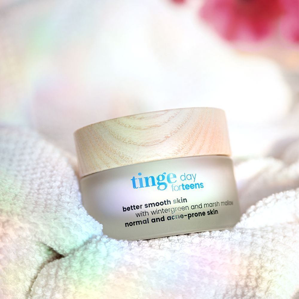 Un pot avec couvercle en bois clair sur une serviette blanche. Inscription: Tinge day for teens, better smooth skin, avec gaulthérie et guimauve, peaux normales et acnéiques.