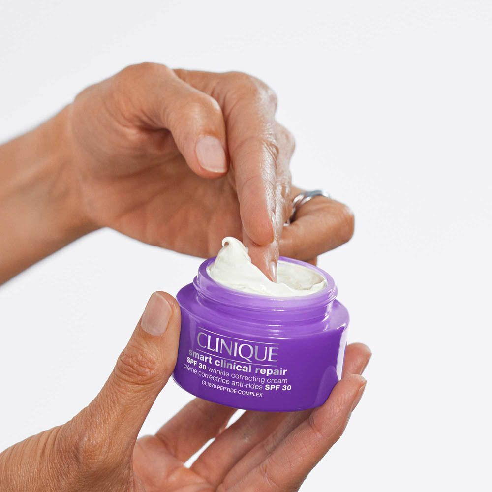 Mains ouvrant un pot violet de crème Clinique Smart Clinical Repair SPF 30.
