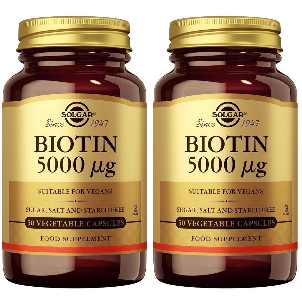 Twee flessen Solgar Biotine 5000 mcg. Bruine glazen flessen met gouden doppen en etiketten. Opschrift: Biotine 5000 mcg, geschikt voor veganisten.