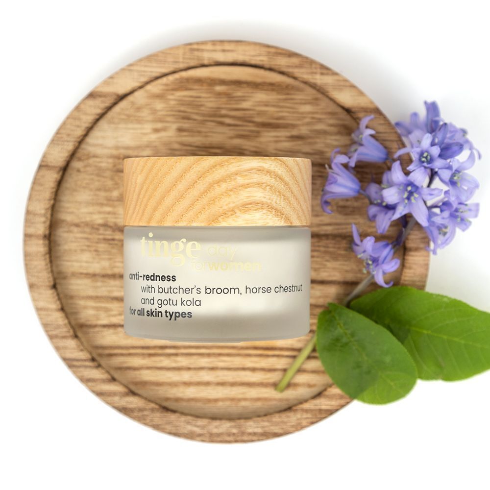 Potje crème anti-roodheid met houten deksel, op houten onderzetter. Blauwe bloemen en bladeren ernaast. Tekst: anti-redness, for all skin types.