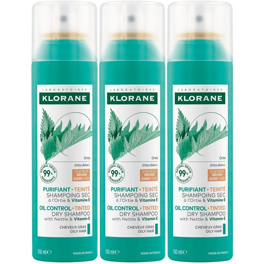 Drie spuitbussen Klorane droogshampoo. Groen-witte etiketten met productinformatie en logo. Bevat brandnetel en vitamine E.