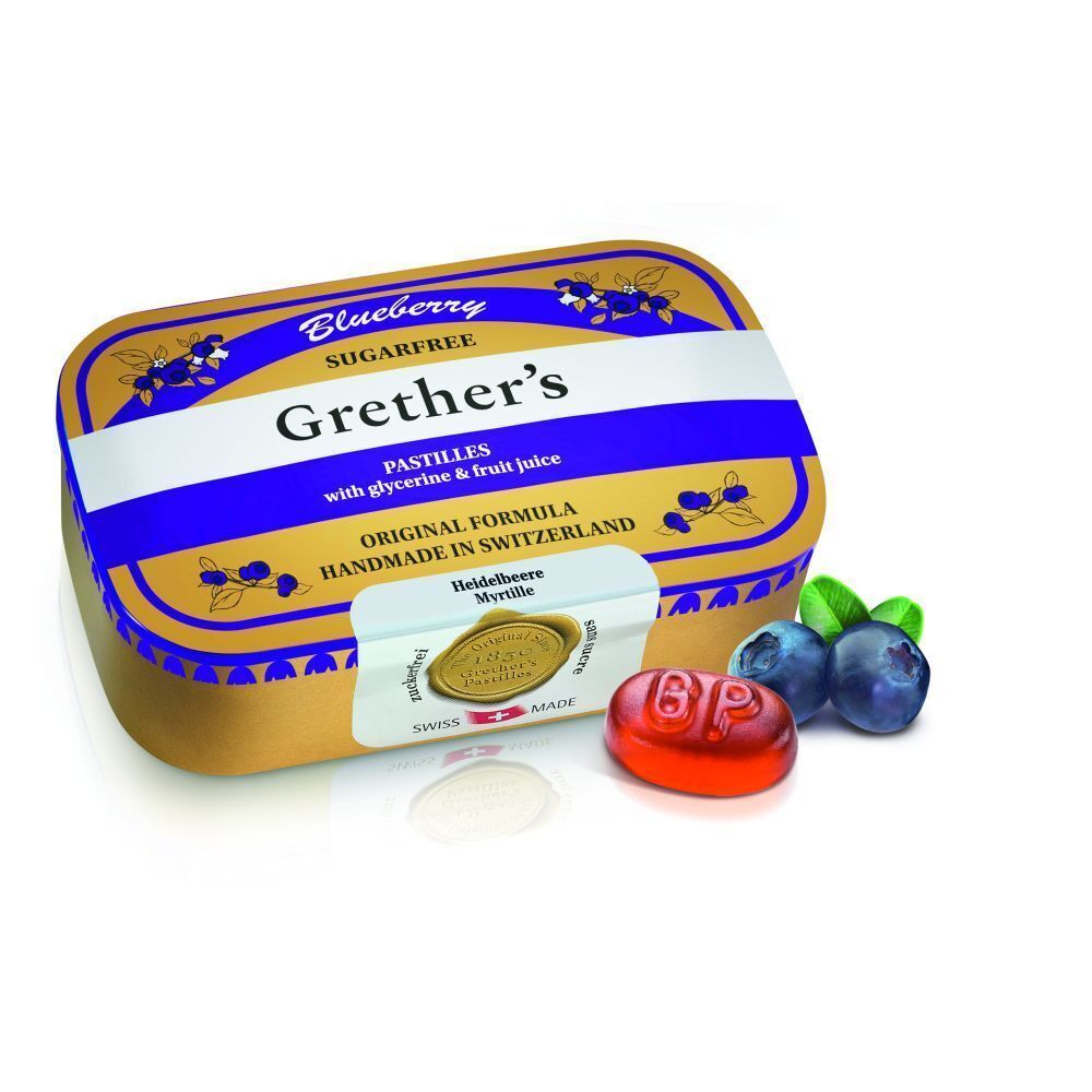 Goudkleurige pastillesdoos met paarse deksel, daarnaast een pastille en bosbessen. Opschrift: Grether's Pastilles Blueberry Sans Sucre.