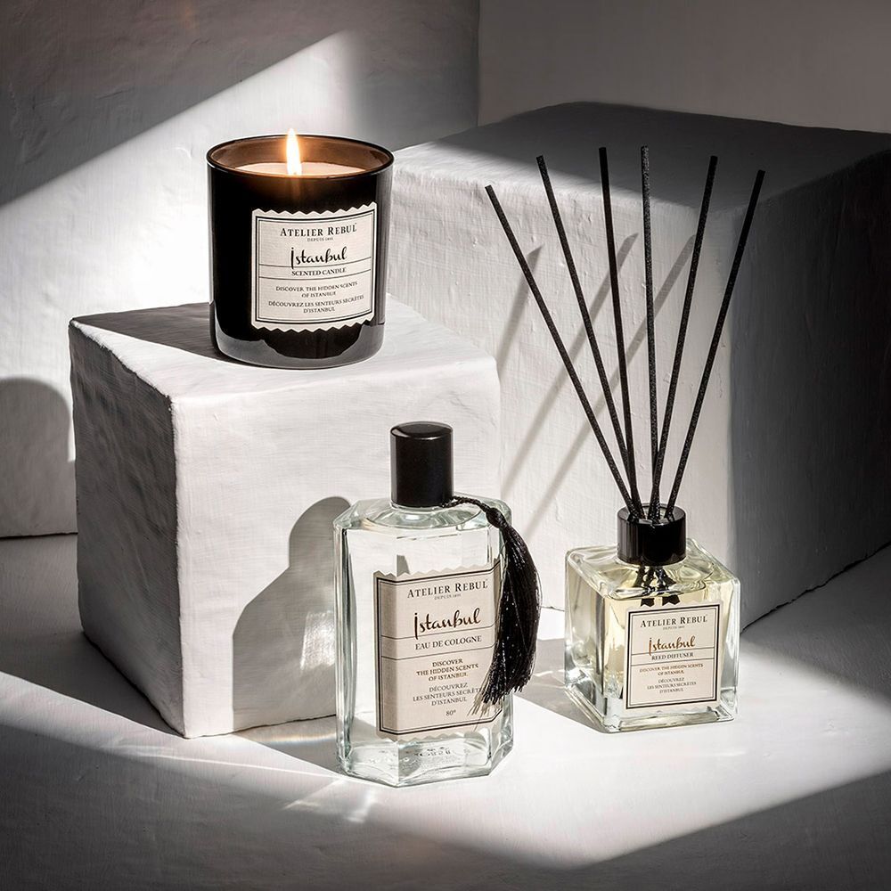 Drie ATELIER REBUL producten: Istanbul Eau de Cologne, geurkaars en geurstokjes. Op een wit voetstuk.