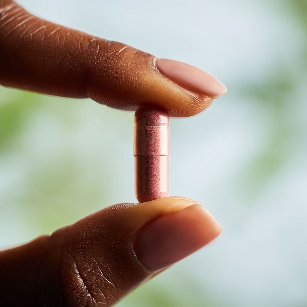 Een roze capsule, vastgehouden door een hand met roze gelakte nagels.