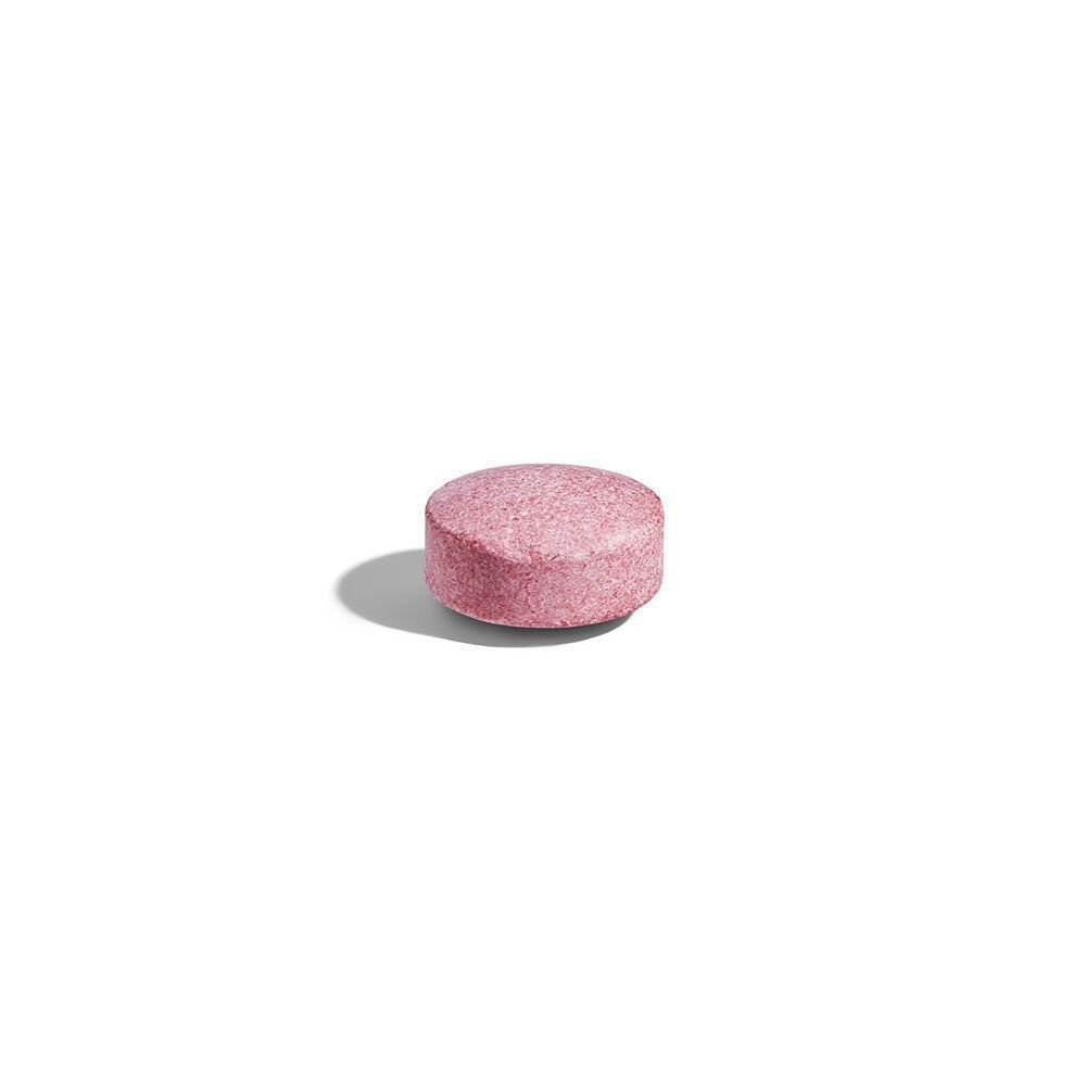 Een enkele, ronde, roze tablet. Op een witte achtergrond.