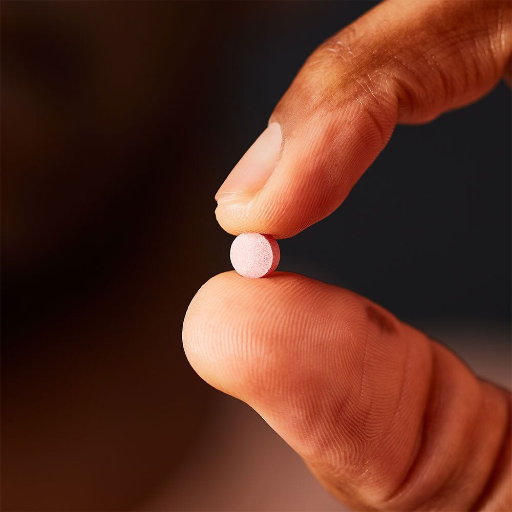 Een roze tablet tussen twee vingers gehouden.