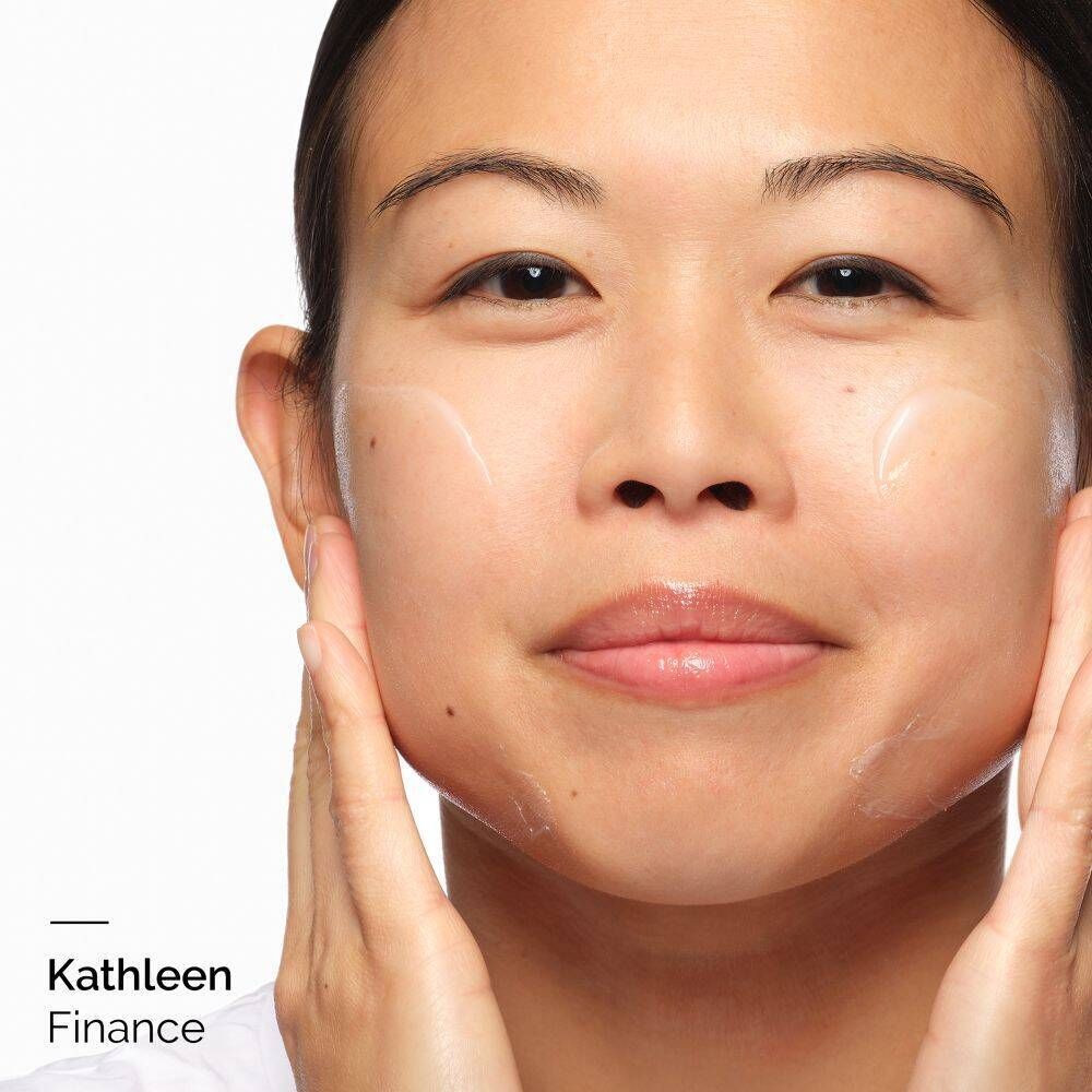 Close-up van een persoon die crème op haar gezicht aanbrengt. De naam 'Kathleen Finance' is linksonder te zien.