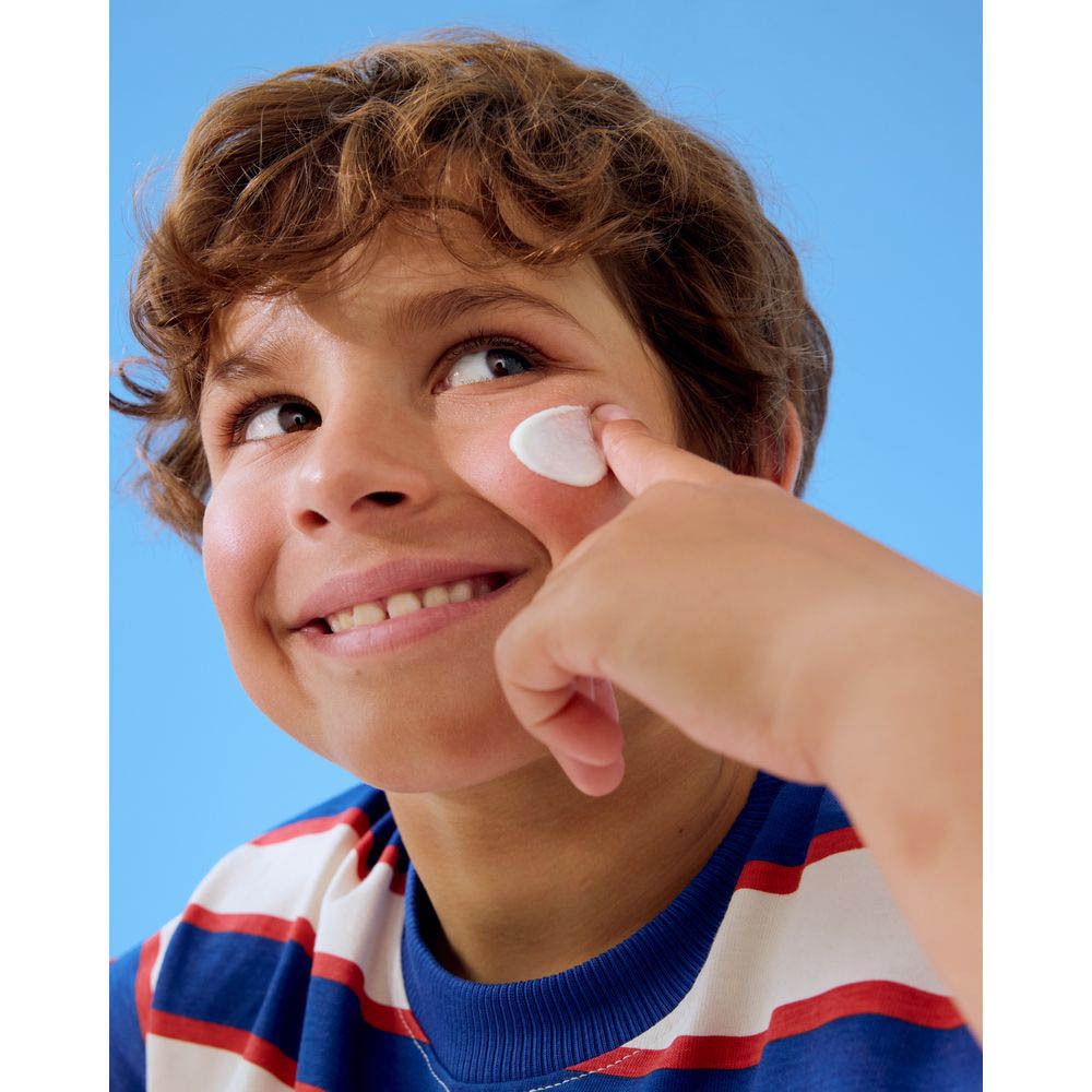 Jongen smeert zonnecrème. Hij draagt een blauw-wit gestreept shirt. Crème op de vinger.