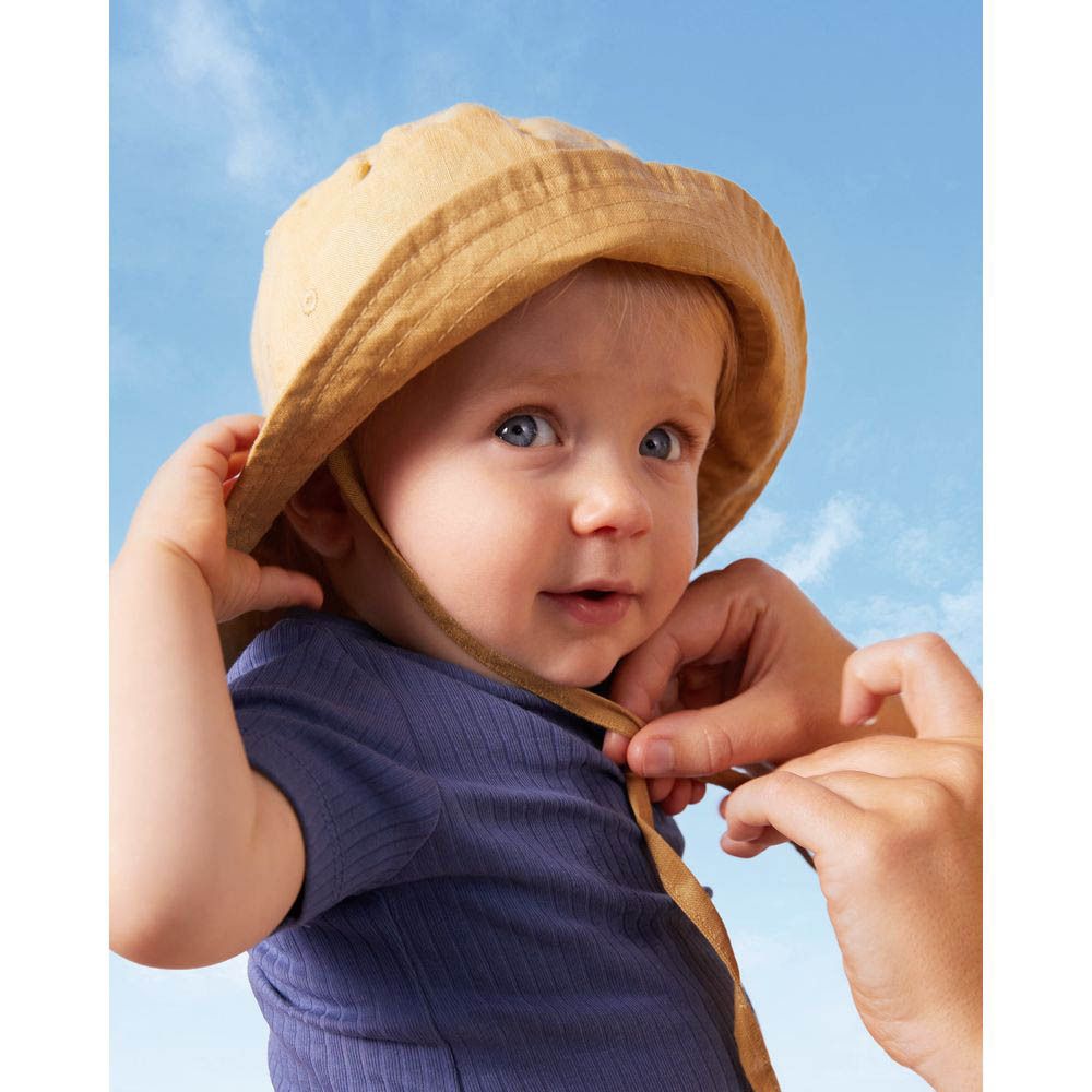 Baby met zonnehoed, handen die de hoed vastmaken. Blauwe lucht op de achtergrond.