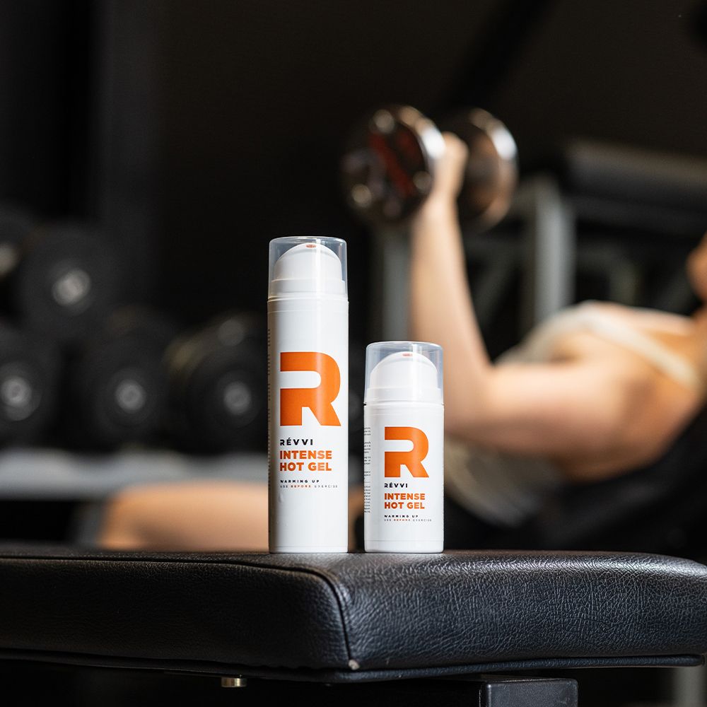 Twee witte cilinders met oranje 'R' en tekst: RÉVVI INTENSE HOT GEL. Transparante pompen. Opschrift: WARMING UP. Persoon traint op de achtergrond.