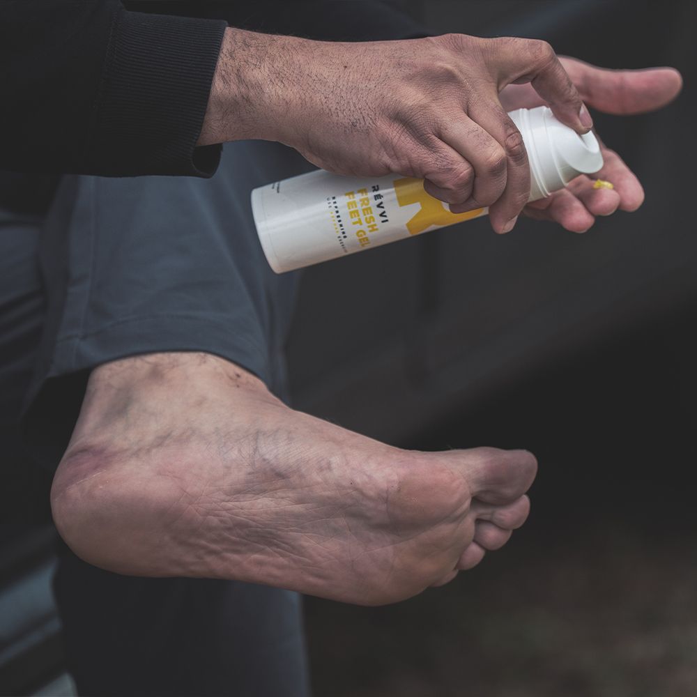 Persoon houdt dispenser vast en brengt gel aan op voet. Witte dispenser met gele "R". Tekst: RÉVVI FRESH FEET GEL.