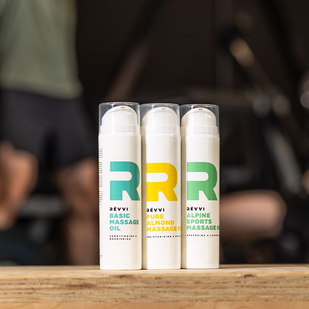 Trois flacons blancs avec logos et texte. Inscription : RÉVVI Basic, Pure Almond, Alpine Sports Massage Oil.