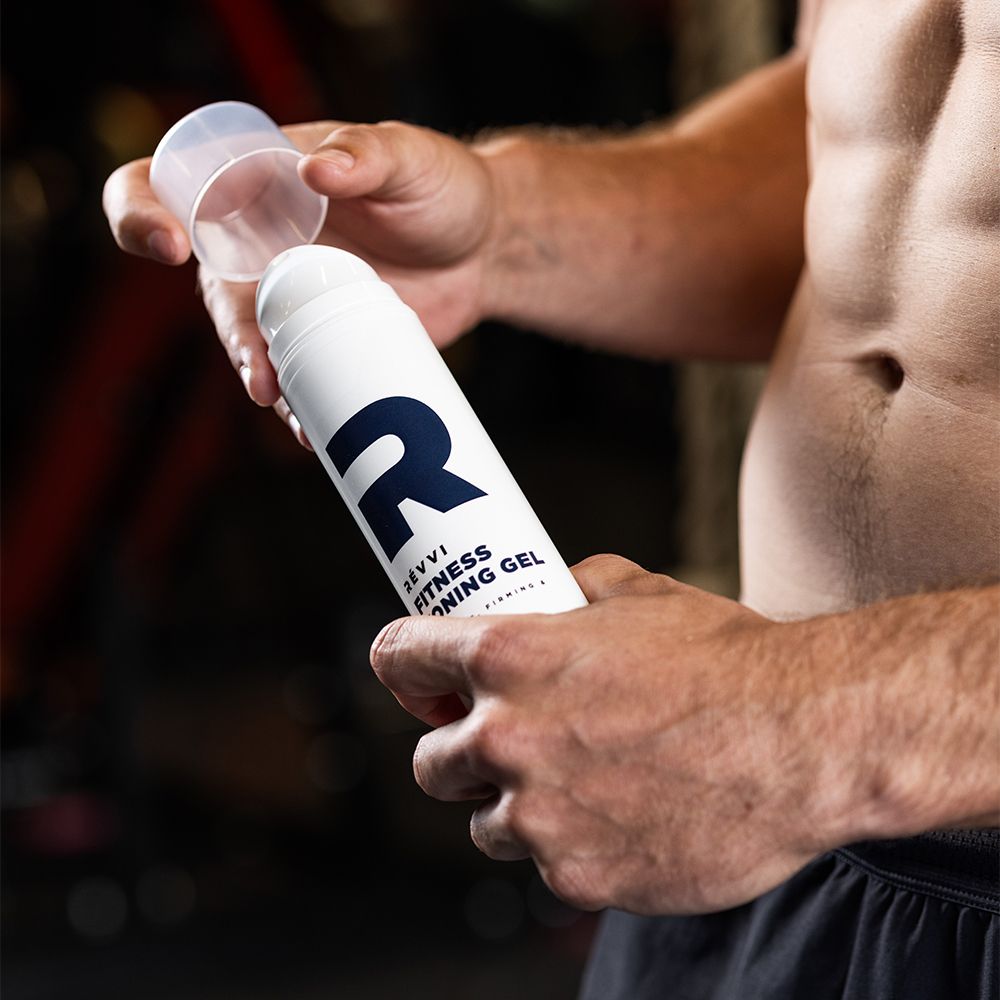 Persoon houdt witte cilinder met blauwe "R" en tekst: RÉVVI Fitness Toning Gel vast. Dop open.