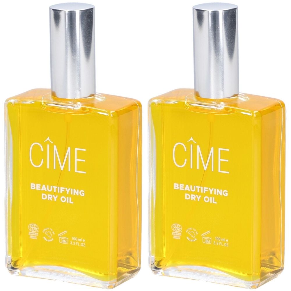 Twee vierkante glazen flessen met zilveren doppen. Op elke fles staat « Cîme Beautifying Dry Oil ».
