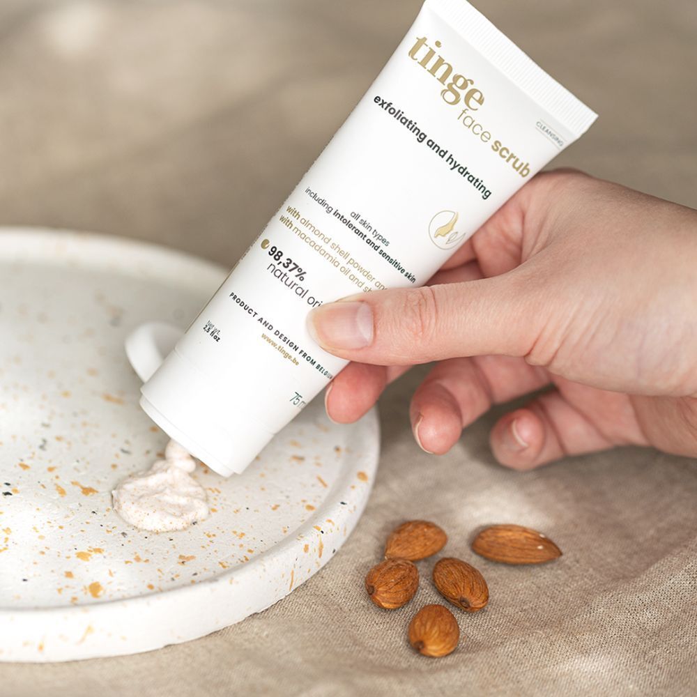 Tube de gommage visage Tinge, contenu sur un support. Amandes à côté. Blanc, avec texte et logo.