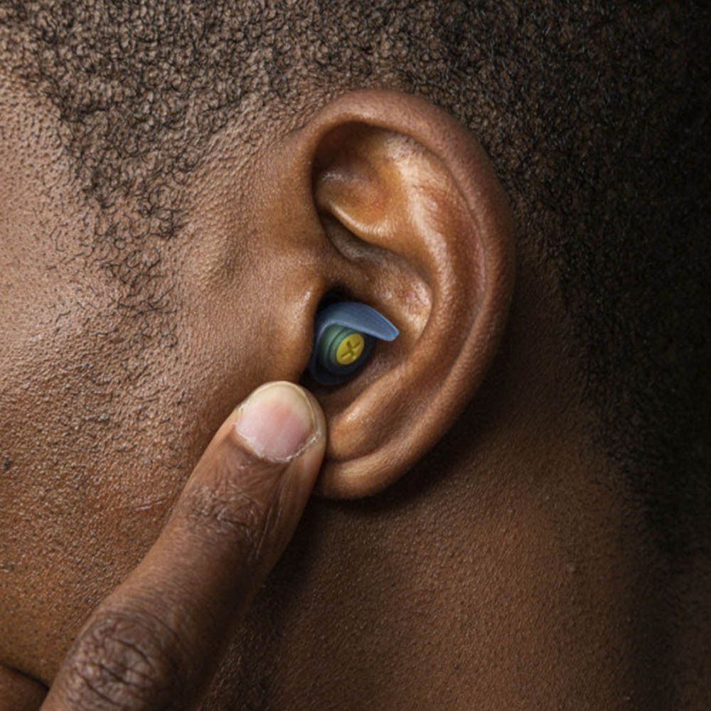 Personne tenant un bouchon d'oreille bleu dans l'oreille. Partie centrale jaune visible.